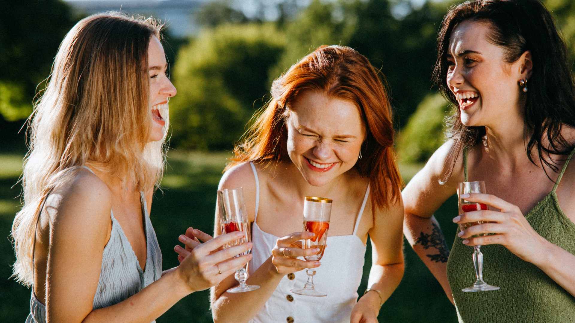 Trzy kobiety na łonie natury śmieją się przy akompaniamencie lampki wina